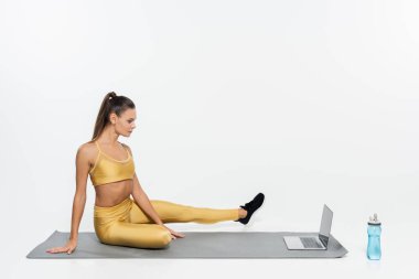 E-spor, spor giyimli bir kadın dizüstü bilgisayar ve şişenin yanında oturuyor, beyaz arka plan.