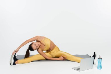E-spor, spor giyimli kadın esneyen ve beyaz arka planda spor minderinde dizüstü bilgisayara bakan. 