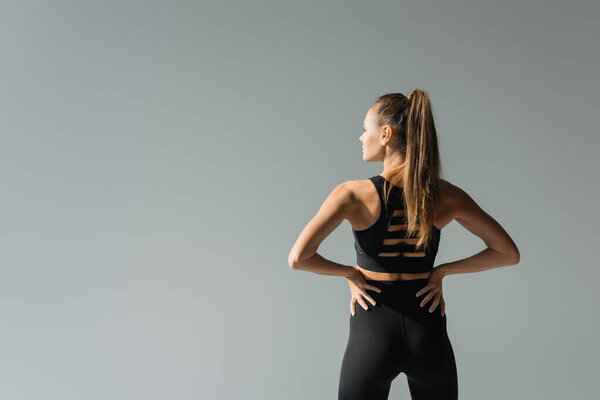 спортсменка, держась за руки на бедрах и стоя изолированно на сером, концепция активного образа жизни, атлетическая 