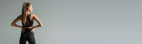 sportswoman with brunette hair in sportive bra and leggings, hands on hips, isolated on grey, banner