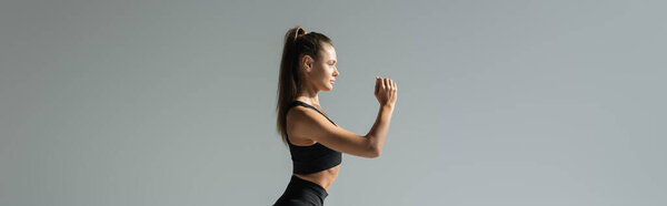 Side view of brunette fit sportswoman working out on grey, banner, active lifestyle concept