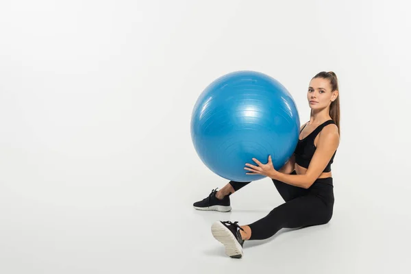 stock image woman in black sports bra holding fitness ball and looking at camera on white background, aerobics 