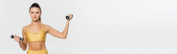 sportswoman in fitness clothing looking at camera, training with dumbbells isolated on white, banner