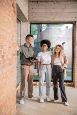 confident real estate agent with folder showing interior of new house to interracial lesbian women clipart