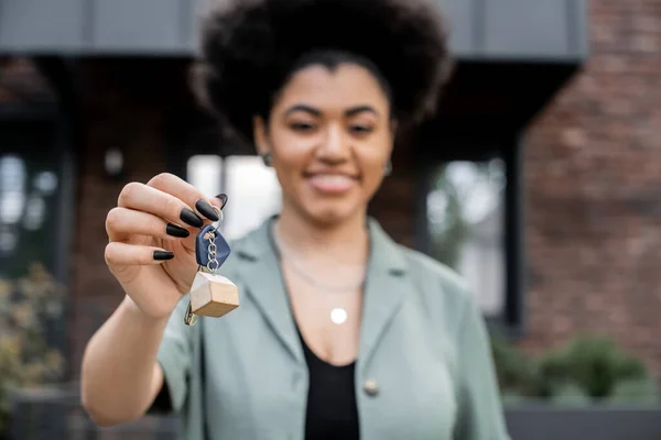 joyful african american property broker holding key from new house on blurred background