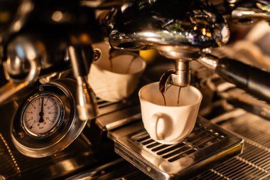 Kahve makinesinden akan kahvenin beyaz bardakta, kafede güneş ışığı olan görüntüsünü kapat.