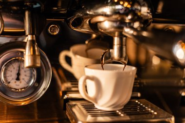 Kahve makinesinden beyaz bardağa dökülen kahvenin yakın görüntüsü. Kafede güneş ışığı var.