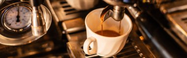Kahve makinesinden beyaz bardağa dökülen kahve manzarasını kapatın. Kafede güneş ışığı, pankart.