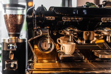 Kahve makinesinden kahve dolduruluyor. Kahve makinesinin yanında. Kafede güneş ışığı var.
