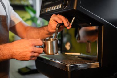 Kahve makinesinde çalışırken kahve makinesinde sütü köpürten barista manzarası.