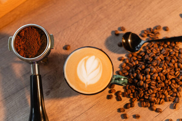 top view of cappuccino in cup near holder and coffee beans on worktop in coffee shop