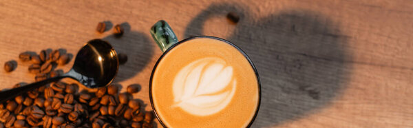 top view of cup of cappuccino near coffee beans and spoon on table in cafe, banner