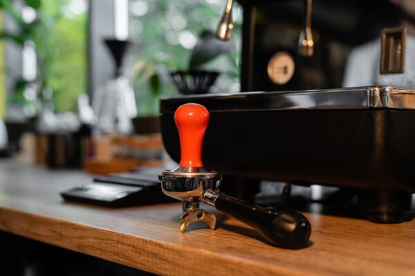 press and holder on worktop near blurred coffee machine in coffee shop on background