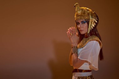 Mısırlı esmer kadın, gölgeli kahverengi arka planda poz verirken kameraya bakıyor.