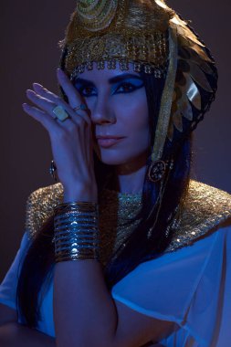 Mısır başlıklı güzel bir kadının portresi. Kahverengi arka planda mavi ışıkta poz veriyor.