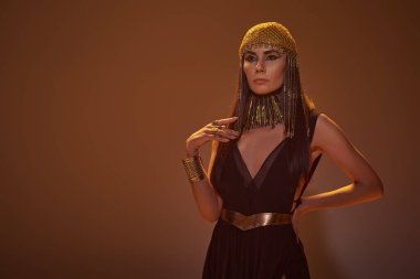 Mısırlı görünümlü ve kolyeli moda kadın kahverengi arka planda dururken el ele tutuşuyor.