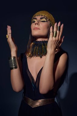 Brunette woman in traditional egyptian attire and headdress posing while standing on blue background clipart