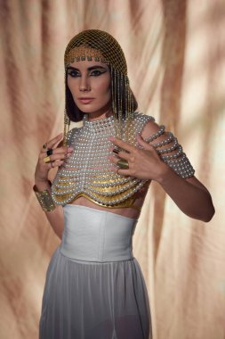 Geleneksel Mısır başlıklı kadın, inci bluzlu ve soyut arka planda poz veren.