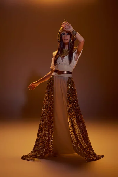 エジプトの外観と茶色の背景に光を当てたヘッドドレスでスタイリッシュな女性の全長 — ストック写真