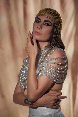 Mısırlı esmer kadın başlıklı, inci bluzlu ve soyut arkaplanda poz veren makyajlı.