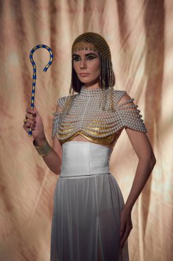 Elegant woman in egyptian look and pearl top holding traditional crook on abstract background clipart