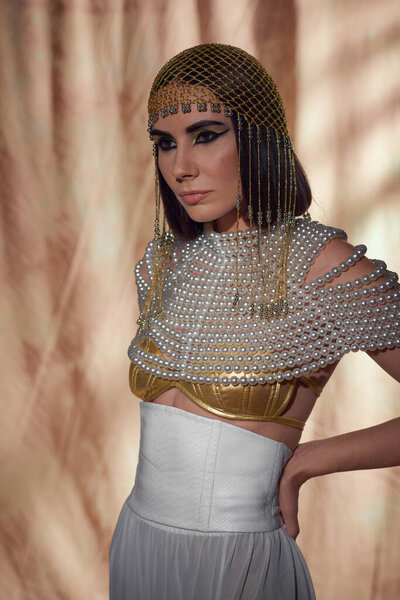 Brunette woman in headdress and egyptian look posing and standing on abstract background