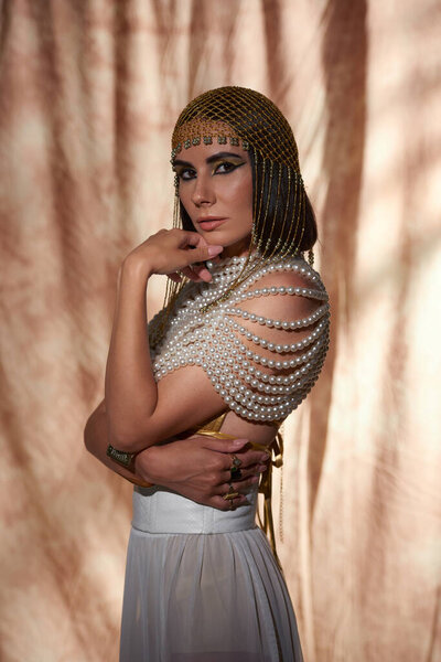 Brunette woman in traditional egyptian headdress and look posing on abstract background