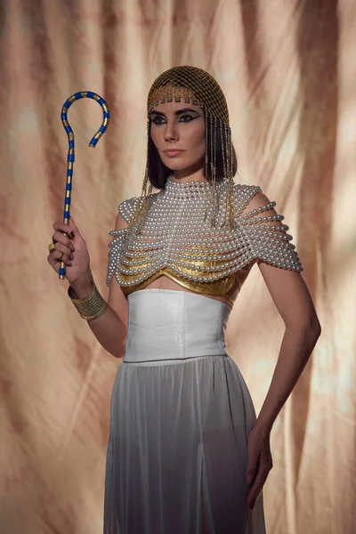 エジプトの外観とパールトップでエレガントな女性 抽象的な背景に伝統的なクロックを保持 — ストック写真
