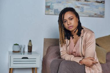 Düşünceli Afrikalı Amerikalı kadın yatakta oturuyor, kendini iyi hissetmiyor, başka tarafa bakıyor, stres, modern yatak odası.