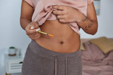 african american woman making hormonal injections in belly, tattoo, pregnancy concept, cropped clipart