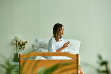 Afro-Amerikan kadın hastane elbisesi içinde elinde haplar, özel koğuş, klinikte hasta, çiçekler.