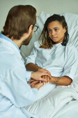 Beyaz önlüklü doktor, Afrikalı Amerikalı bir kadının elini tutuyor, rahat, özel koğuş, düşük