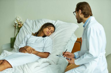 Dosyası olan sakallı doktor üzgün Afrikalı Amerikalı bir kadının yanında duruyor, özel koğuşta.
