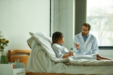 Afrika kökenli Amerikalı bir hastanın yanında elinde ilaç şişesi olan özel koğuşta ilaç yazan bir doktor.