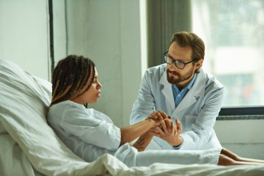 doctor holding hands of sad african american woman, comforting patient, private ward in hospital clipart