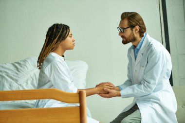 Sakallı doktor, Afrikalı Amerikalı bir kadının elini tutuyor. Rahatlatıcı bir hasta, özel koğuş, hastane.