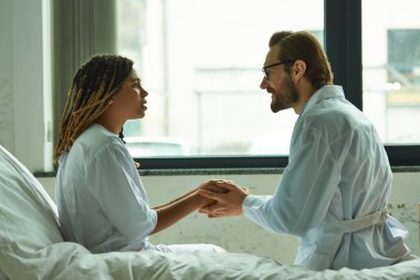 Afro-Amerikan kadınını rahatlatan doktor, hastanın elini tutuyor, özel koğuş, hastane, gülümseme.