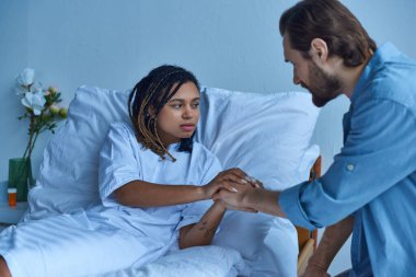 Düşük, depresyondaki Afrikalı Amerikalı kadın kocasıyla el ele tutuşuyor, keder, hastane koğuşu.