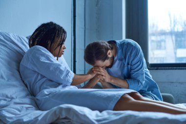 Düşük, depresyondaki Afrikalı Amerikalı kadın yas tutan kocanın elini tutuyor, hastane koğuşunda.