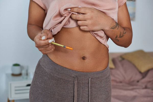african american woman making hormonal injections in belly, tattoo, pregnancy concept, cropped