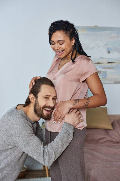 happy man listening belly of pregnant african american wife, fertility, couple, future parents