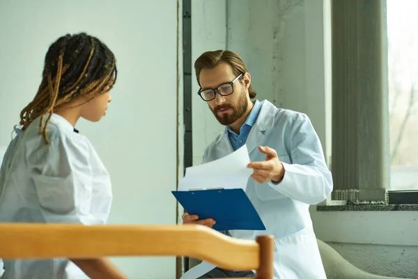 stock image doctor in glasses looking at diagnosis on clipboard, african american woman, private ward