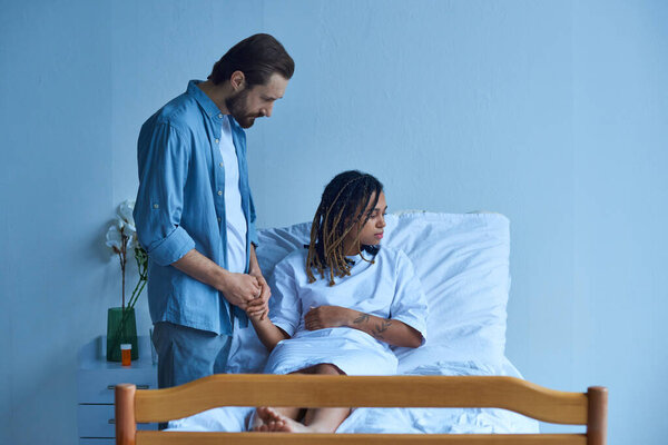 концепция выкидыша, мужчина держит за руку африканскую американскую жену, утешает, больничный пациент