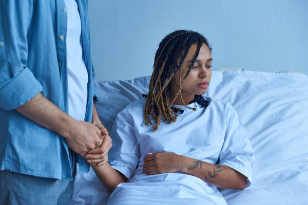 miscarriage concept, man holding hand of depressed african american wife, comforting, hospital