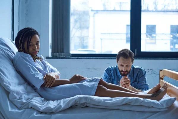 stock image miscarriage concept, man grieving near depressed african american woman, hospital, private ward