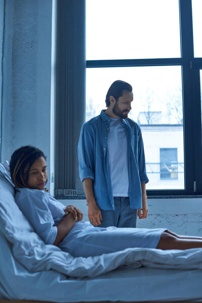 Концепция выкидыша, грустный человек, стоящий рядом с африканской американской женой, горе, больничная койка в частном отделении