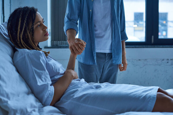 Концепция выкидыша, мужчина держит за руку грустную африканскую американскую жену, горе, больничную койку личное отделение
