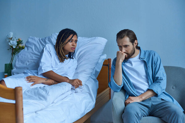 депрессивный мужчина сидит рядом с больной африканской женой, больницей, частной палатой, скорбью, клиникой