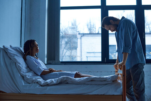 мужчина, скорбящий рядом с подавленной африканской женой-американкой, стоящий рядом с больницей, концепция выкидыша