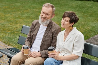 Mutlu yaşlı adam ve kadın bankta oturuyor, ellerinde kağıt bardaklarla kahve, yaşlı çift, romantizm
